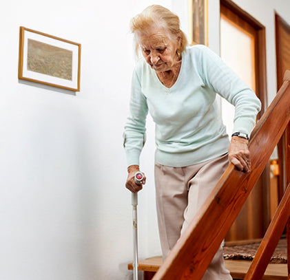 An old woman coming down the stairs holding her stick.
